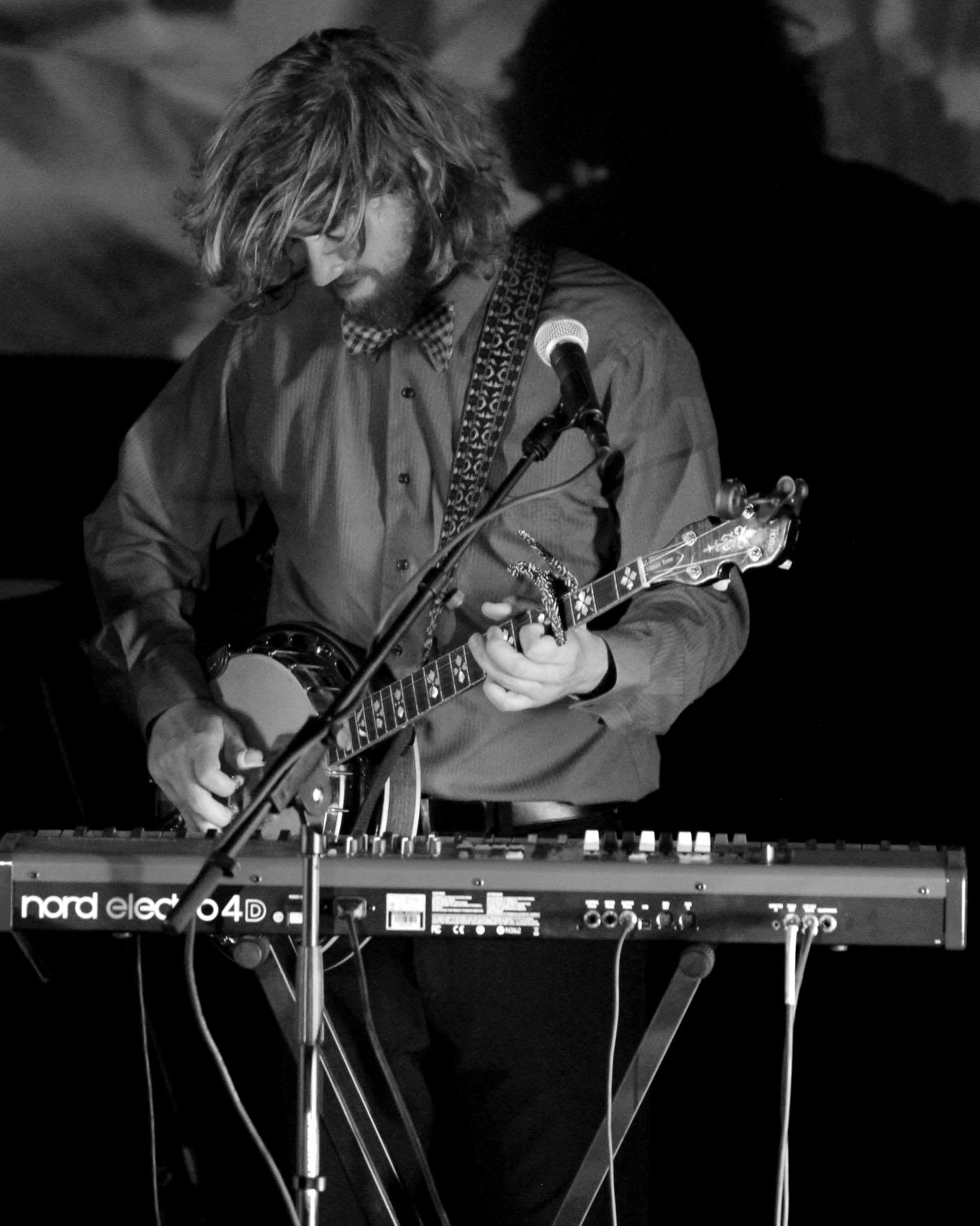 Tyler Rice playing banjo over a keyboard in warm light
