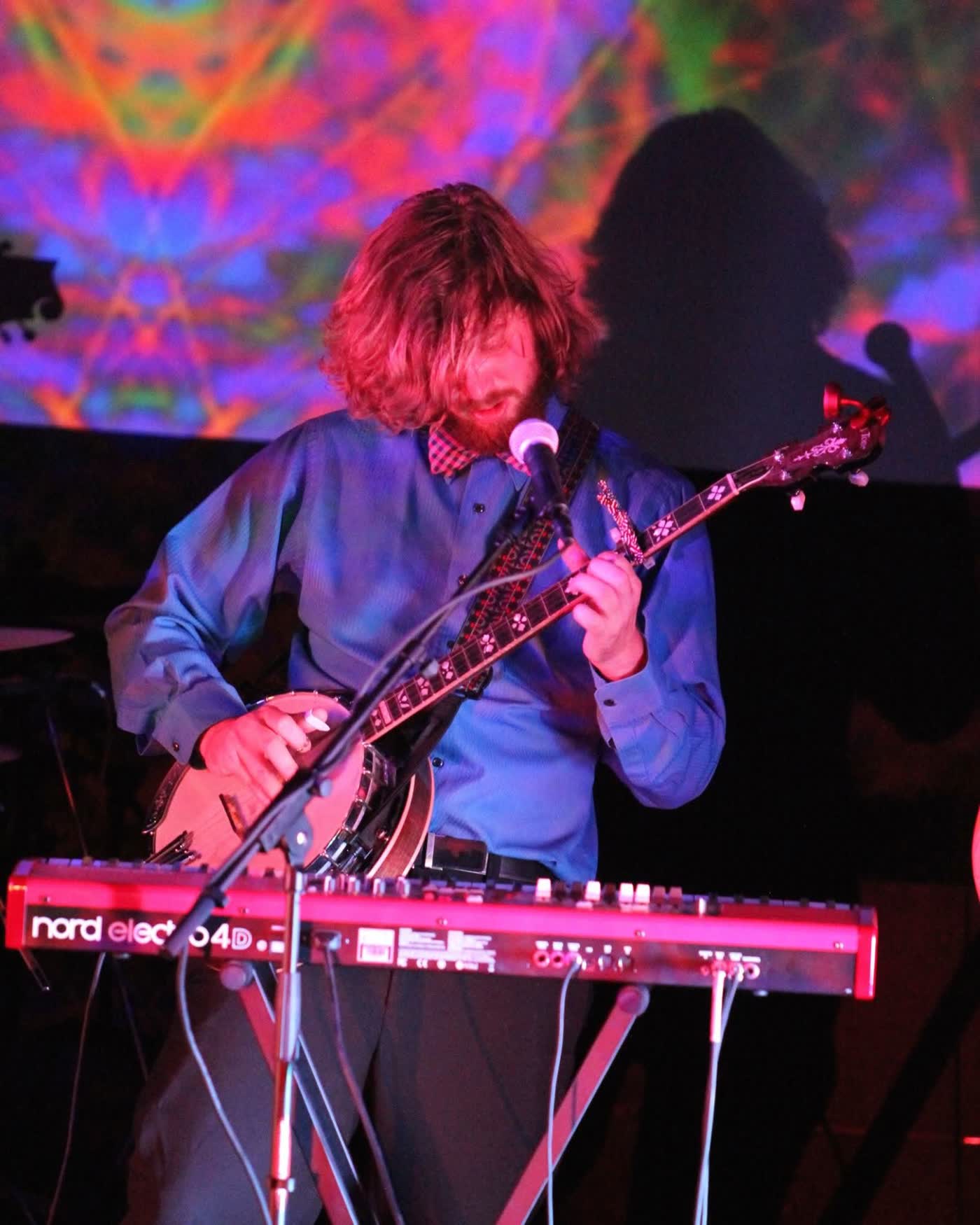Color close-up of Tyler Rice playing a 5-string banjo resting on a red keyboard