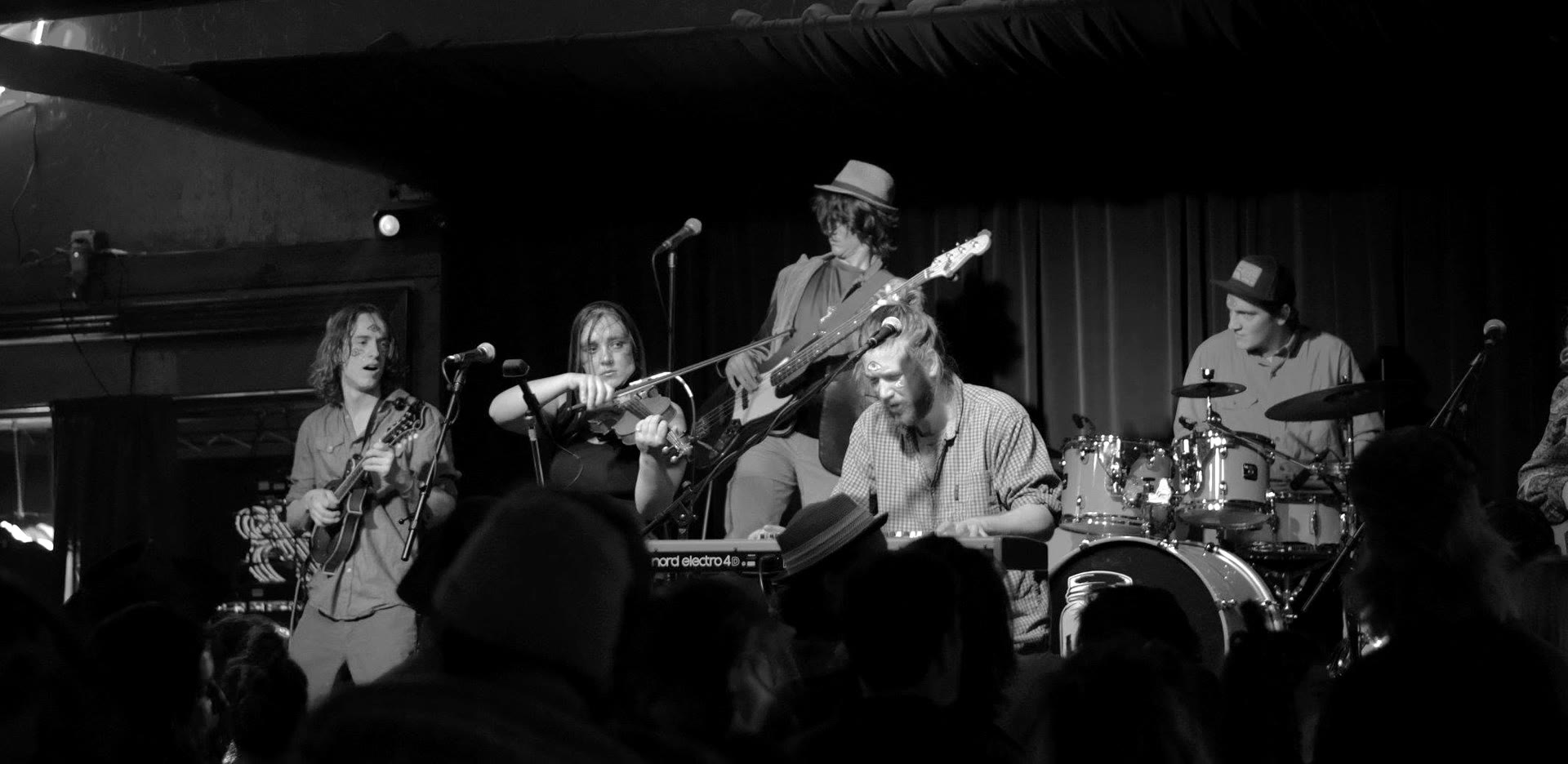 Tyler Rice playing banjo at night in a patched tan jacket
