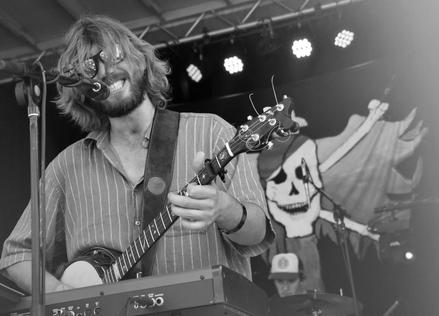 Tyler Rice playing banjo over a red keyboard in front of a skull backdrop, black and white