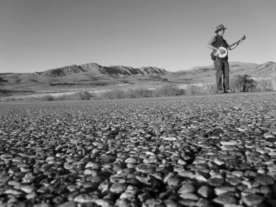 Tyler Rice playing banjo alone on an empty desert highway