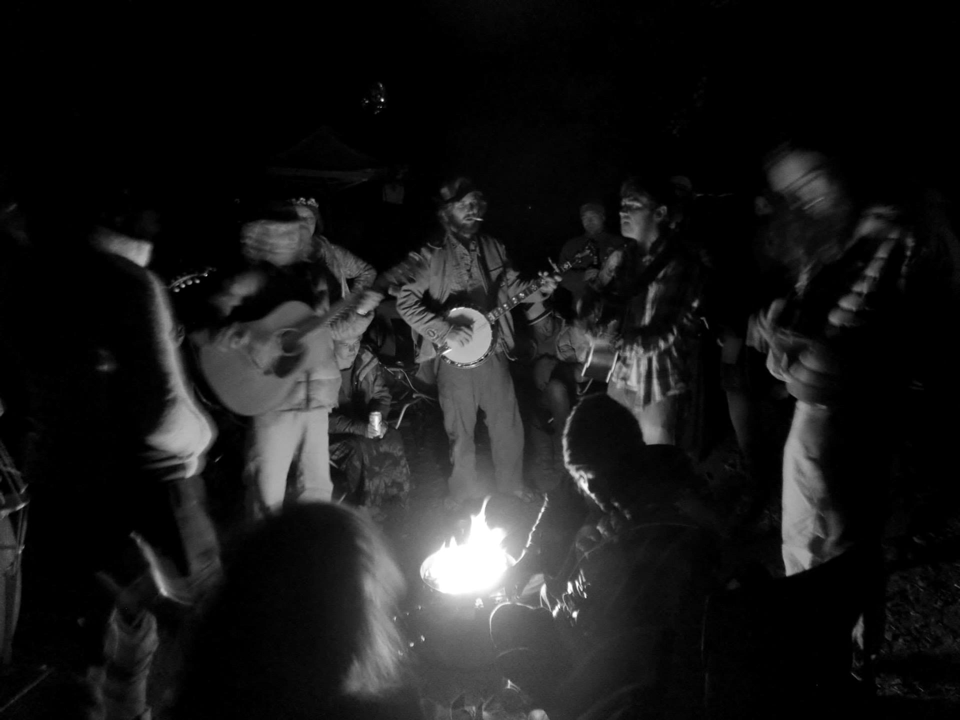Tyler Rice playing banjo at a nighttime campfire circle