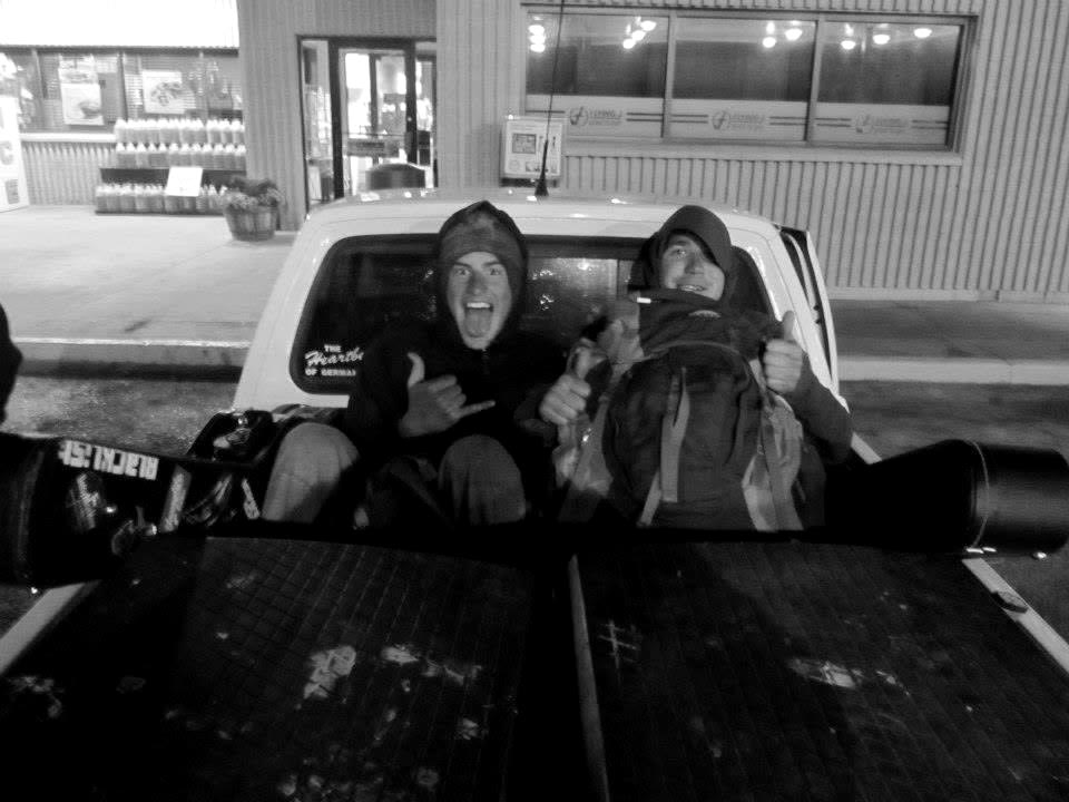 Two men giving thumbs-up in a truck bed loaded with snowboards at night
