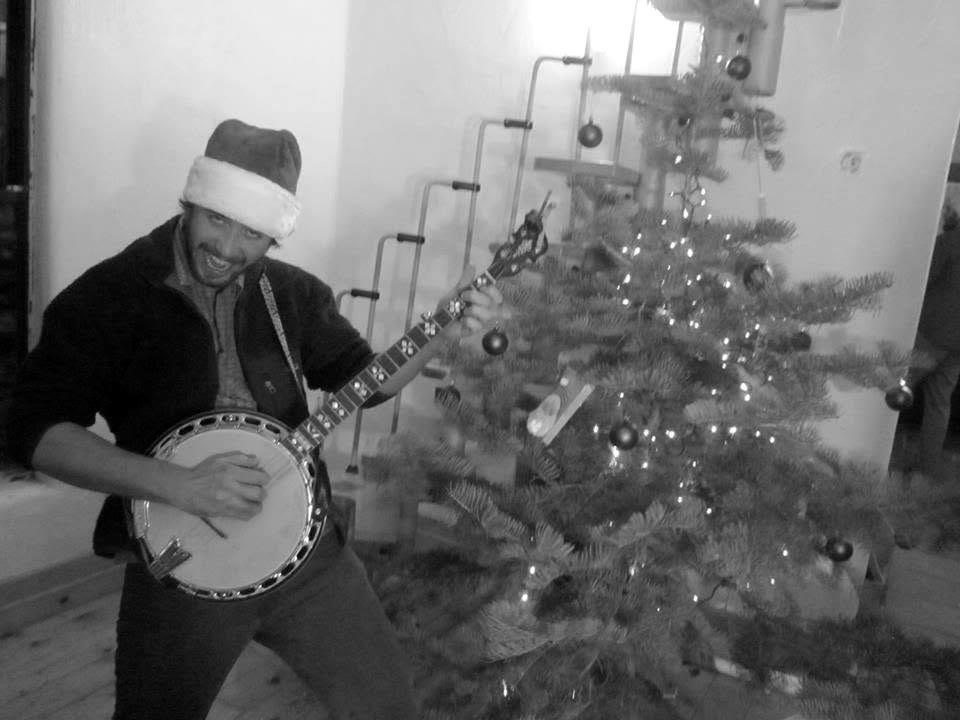 Tyler Rice mugging with his banjo in a Santa hat beside a Christmas tree